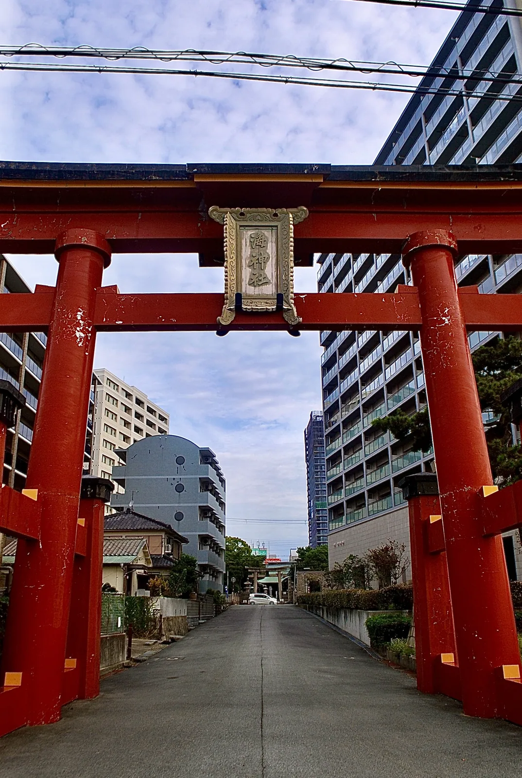 朱色の大きな鳥居をくぐり、まっすぐのびる道とマンション