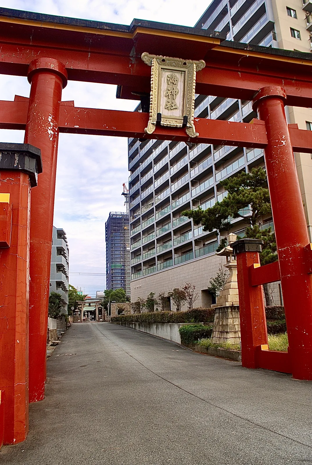 大きな朱色の鳥居を見上げ、奥に高層マンションが見える風景