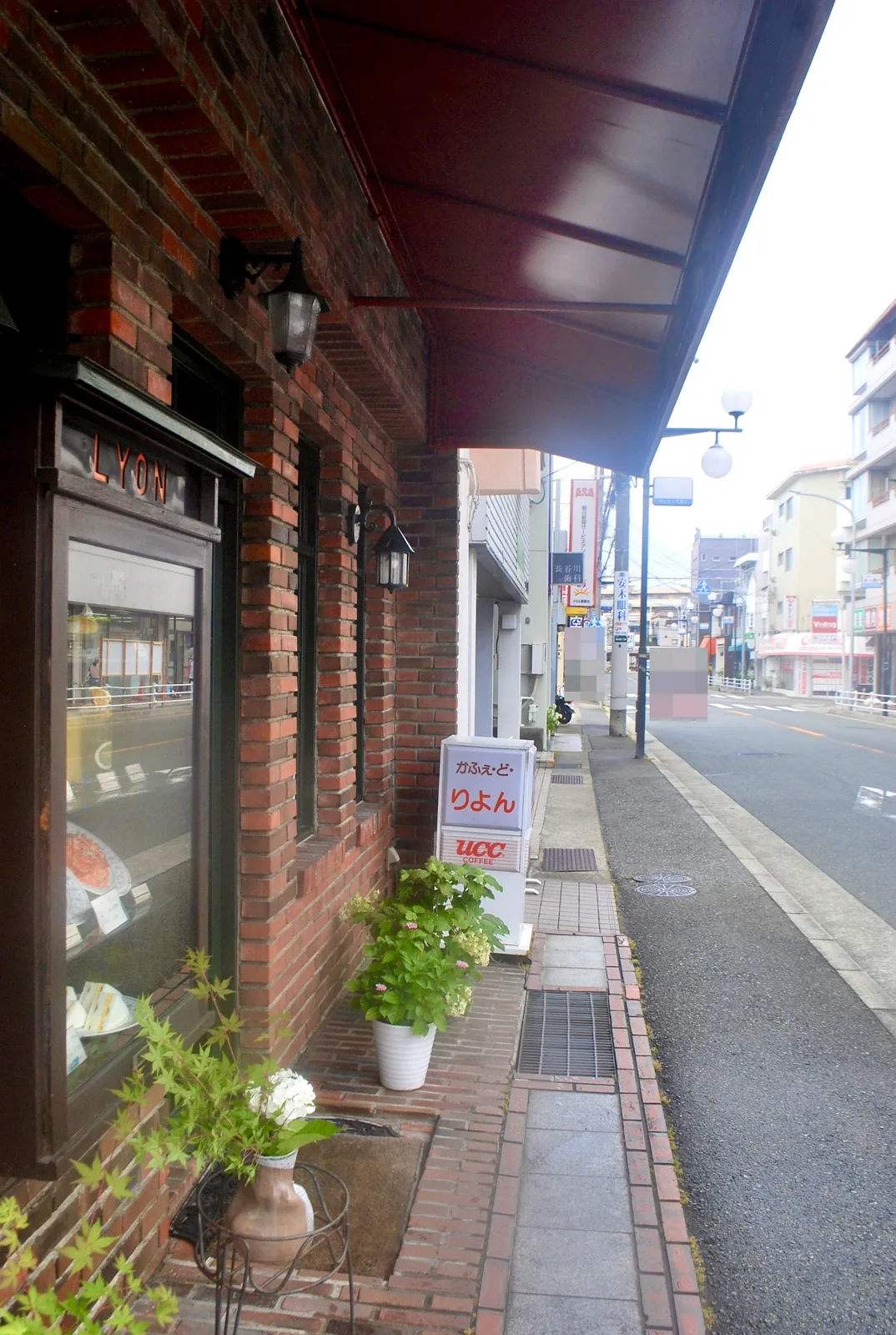 レンガの壁と「かふぇ・ど・りよん」の看板が並ぶ、大通り沿いの歩道