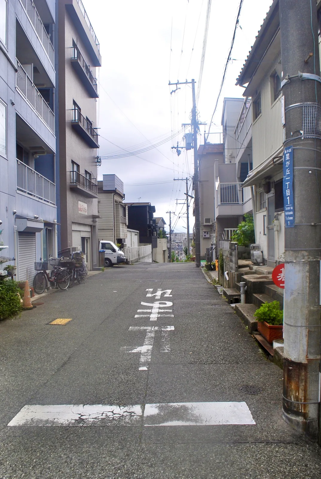 電柱と家々が並び、坂の上へまっすぐ続く住宅街の道