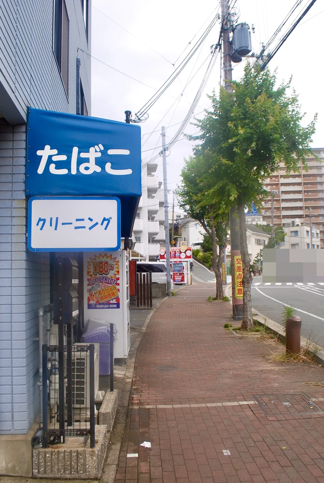 青い「たばこ」の看板と、並木の続く大通り沿いの歩道