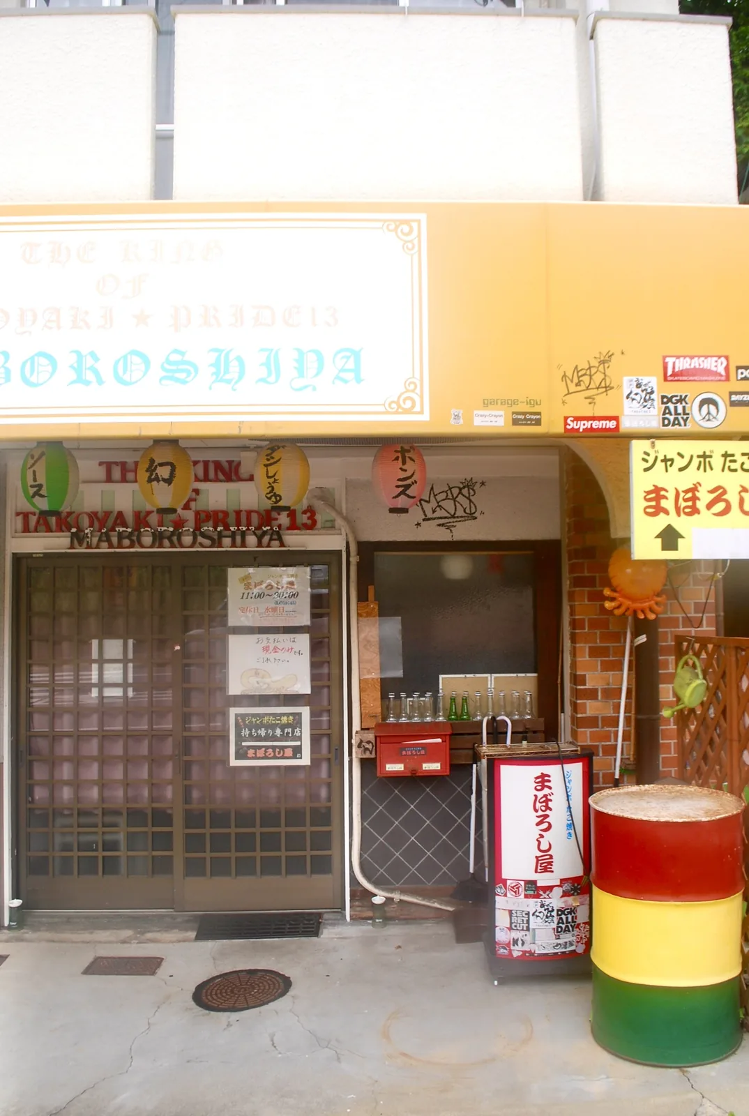 ちょうちんとドラム缶のある、にぎやかなたこ焼き屋の店先
