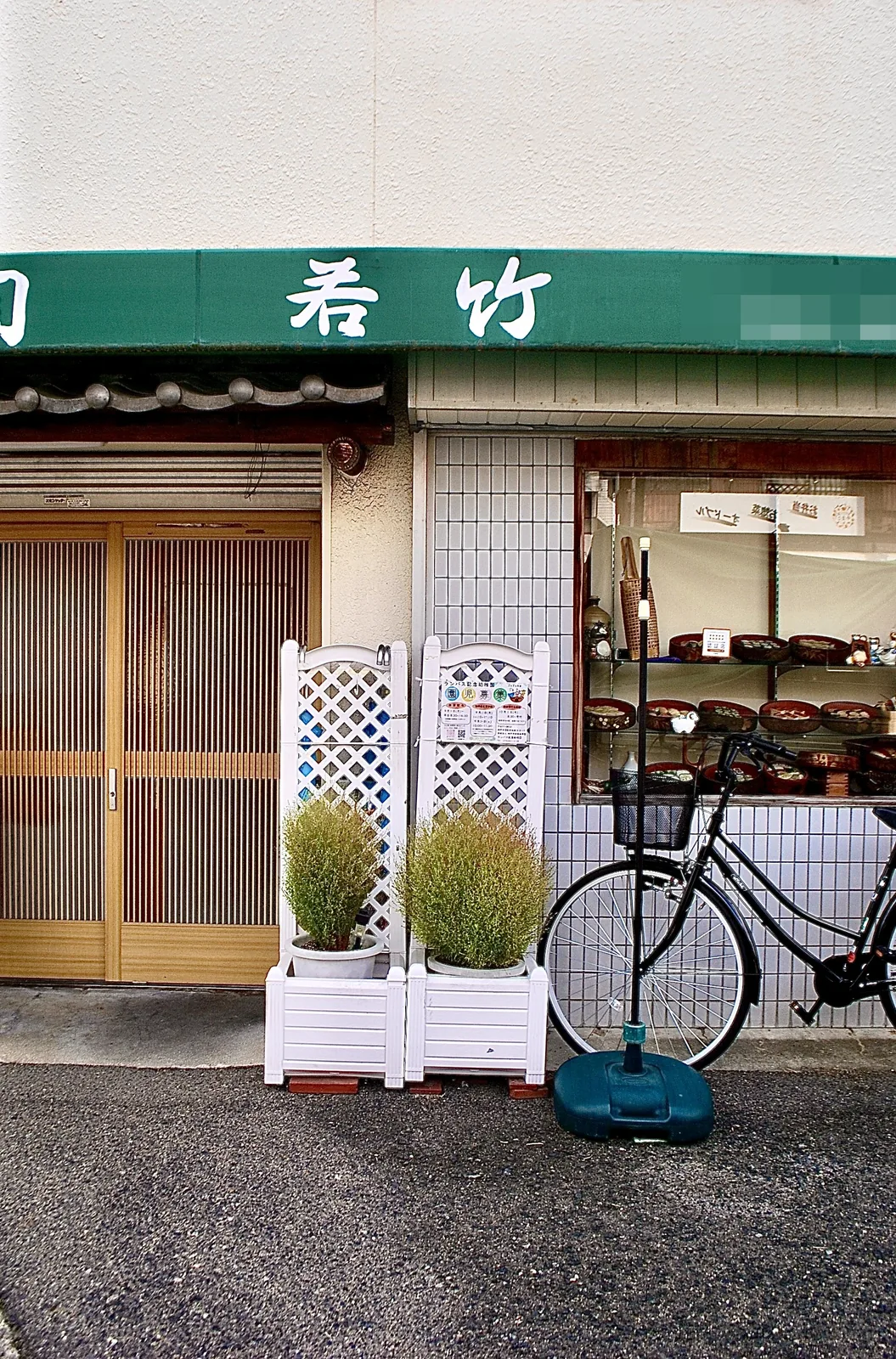 緑の日よけと格子戸、白い花台が並ぶ寿司屋の店先