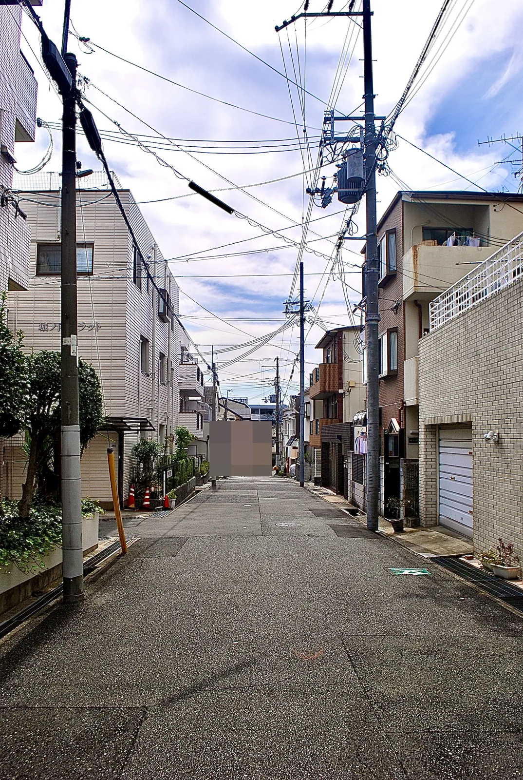 電柱と家々のあいだを、奥までまっすぐ続く住宅街の道