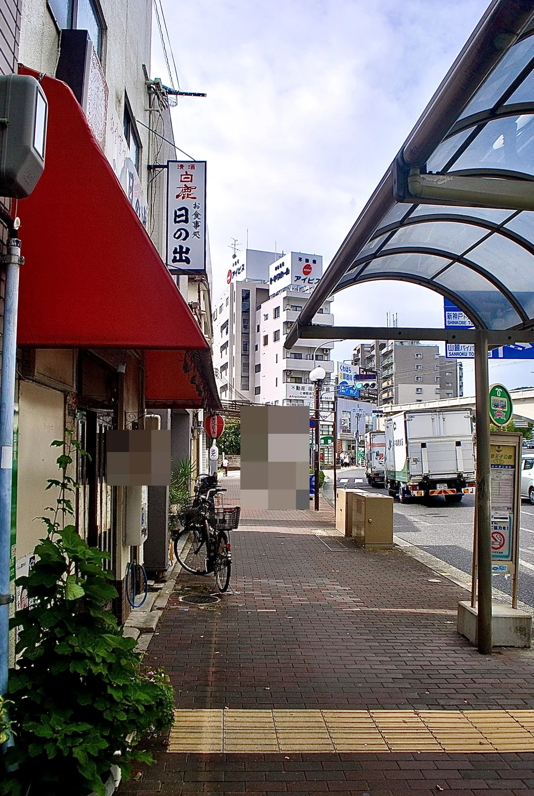 赤い日よけの店と、屋根つきのバス停が並ぶ大通りの歩道