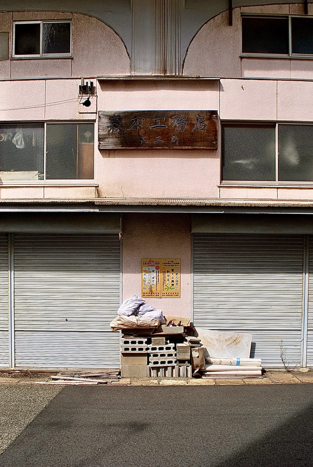 アーチの壁と古い木の看板、シャッターが残る建物