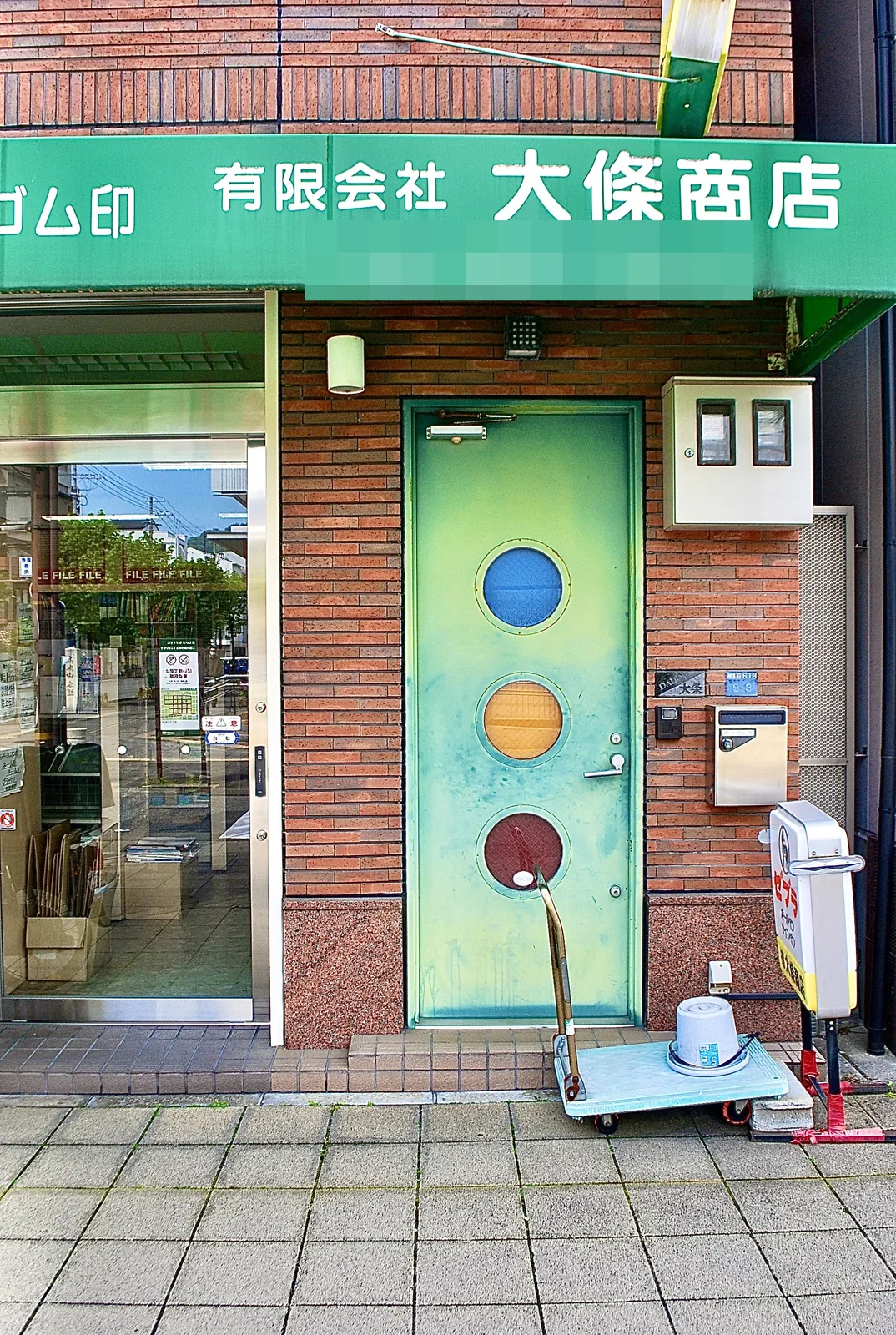 青・黄・赤の丸い窓が並ぶ緑の扉と、レンガの壁