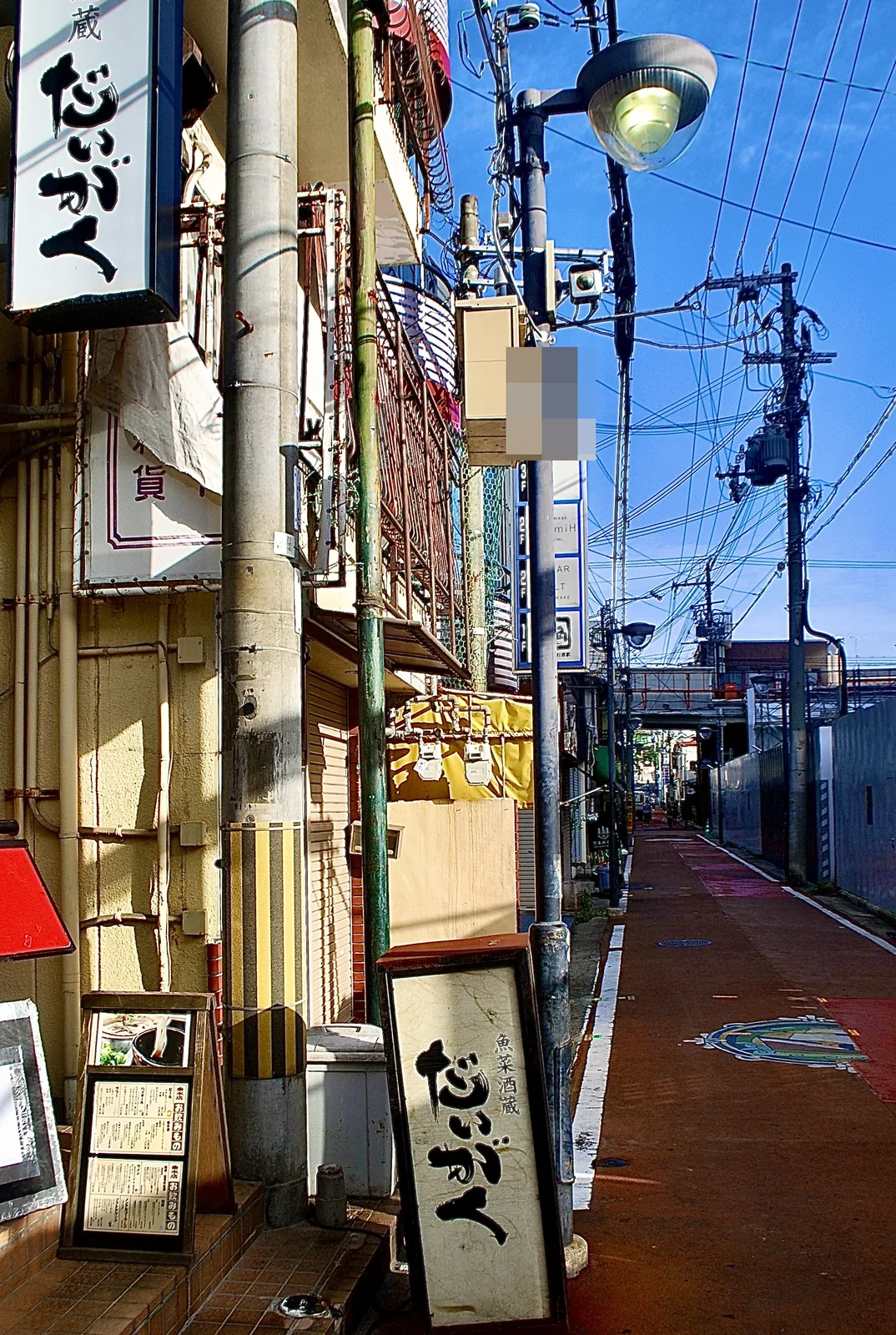 居酒屋の木の看板の先に、赤い舗装の道がまっすぐ続く風景