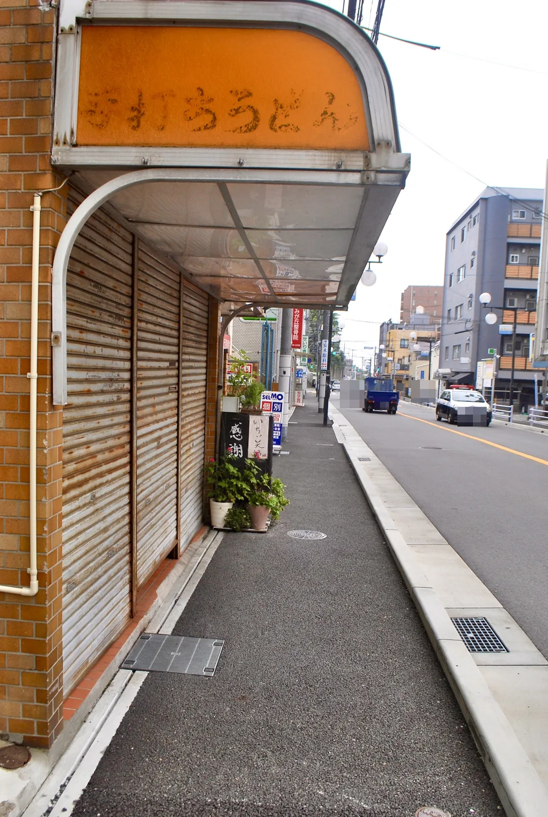 オレンジの看板のうどん店の前から、大通りへ続く歩道
