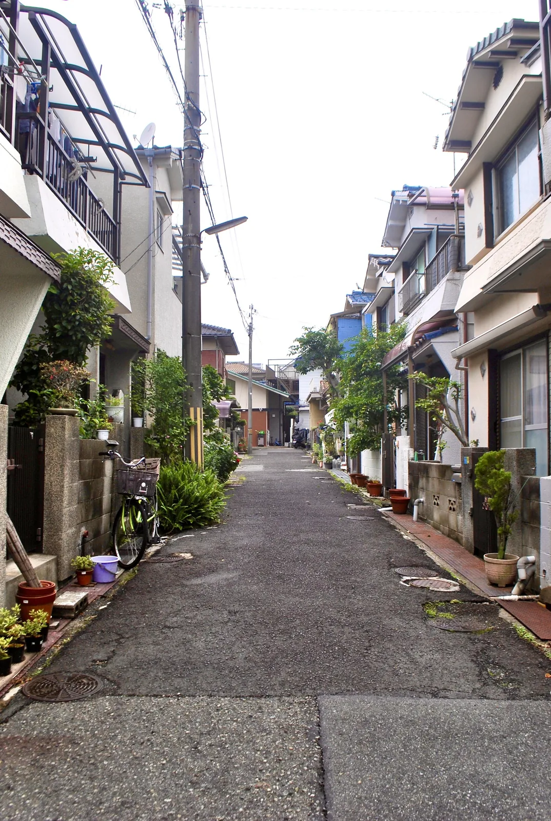 植木鉢や自転車が並ぶ、家々のあいだの細い路地
