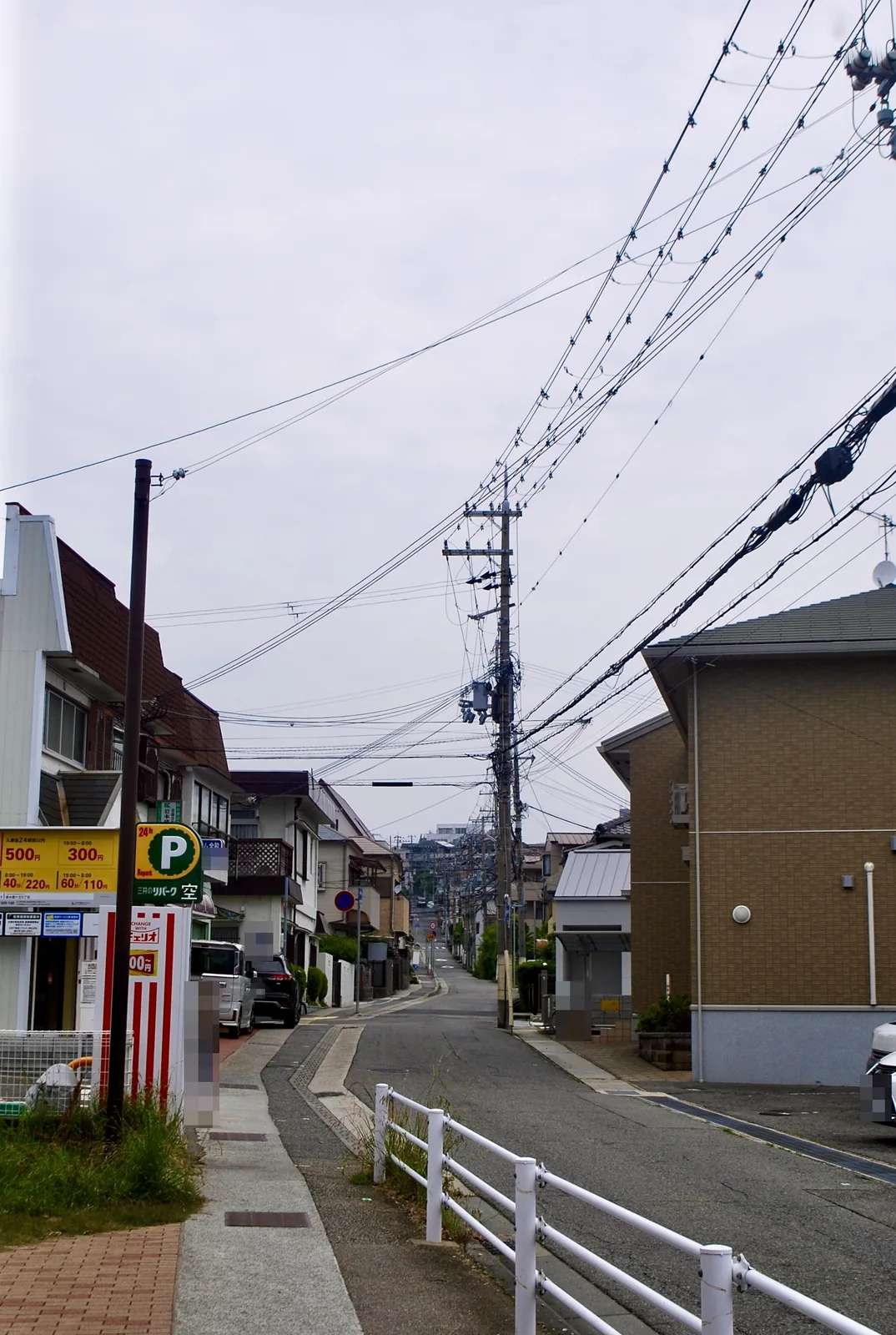 駐車場の看板と白い柵の先に、カーブしながら続く坂道