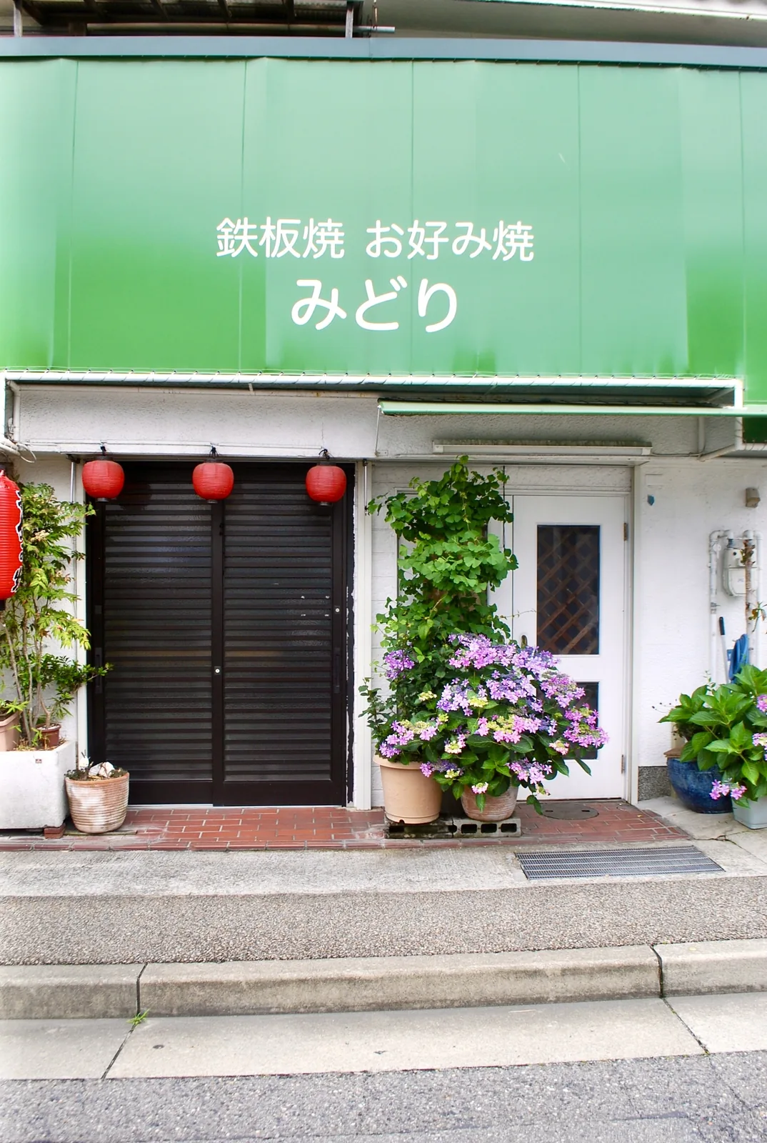 赤い提灯が下がる黒い扉と、あじさいの鉢植えが並ぶ店の入口