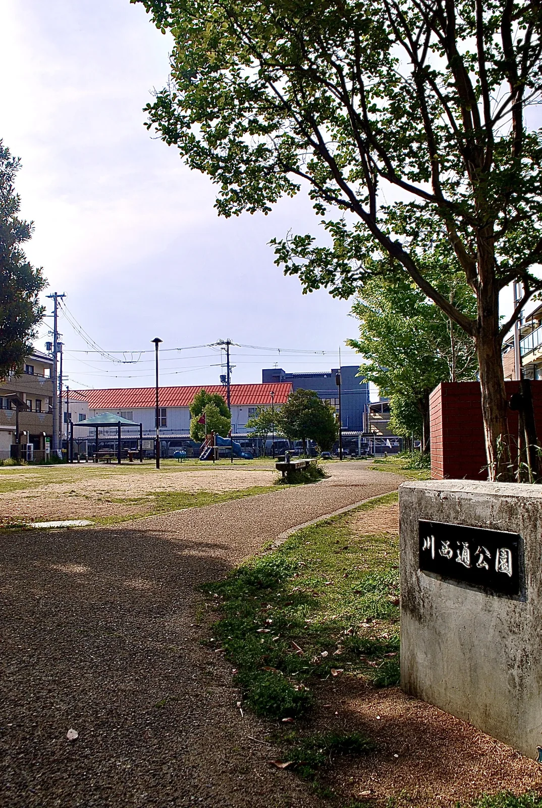 「川西通公園」の石の銘板と、広場の向こうの遊具