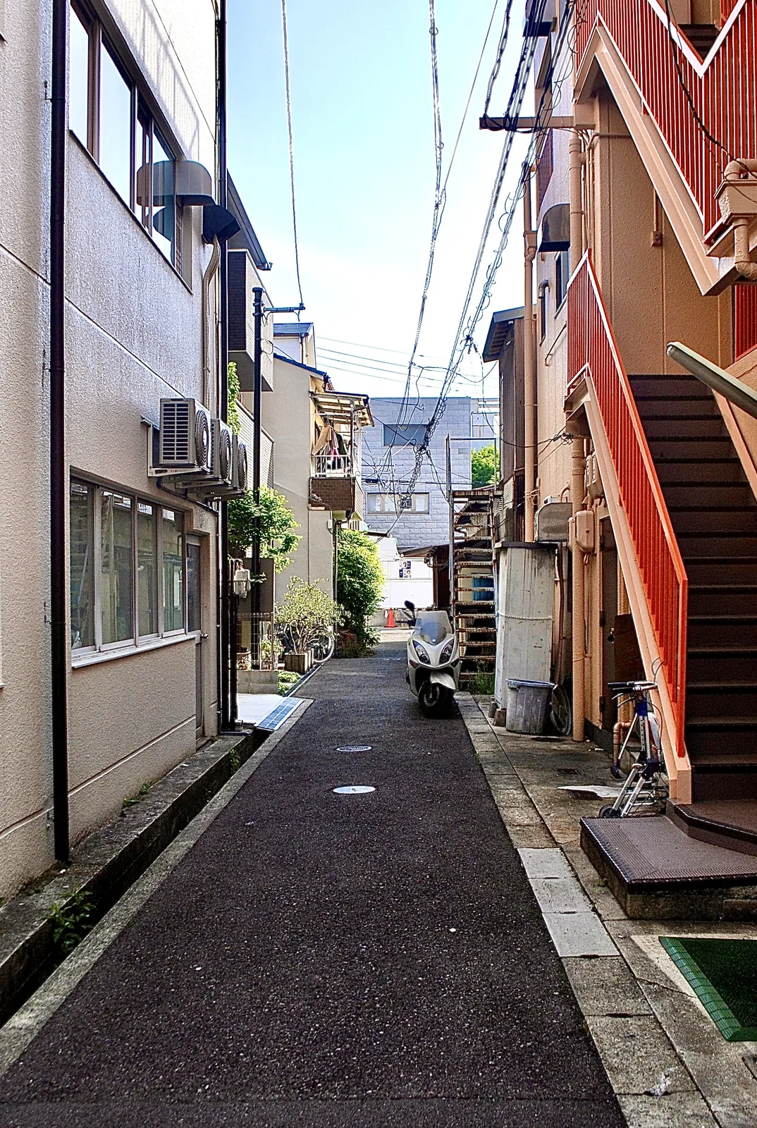 オレンジの外階段の家と、奥へ続く細い路地