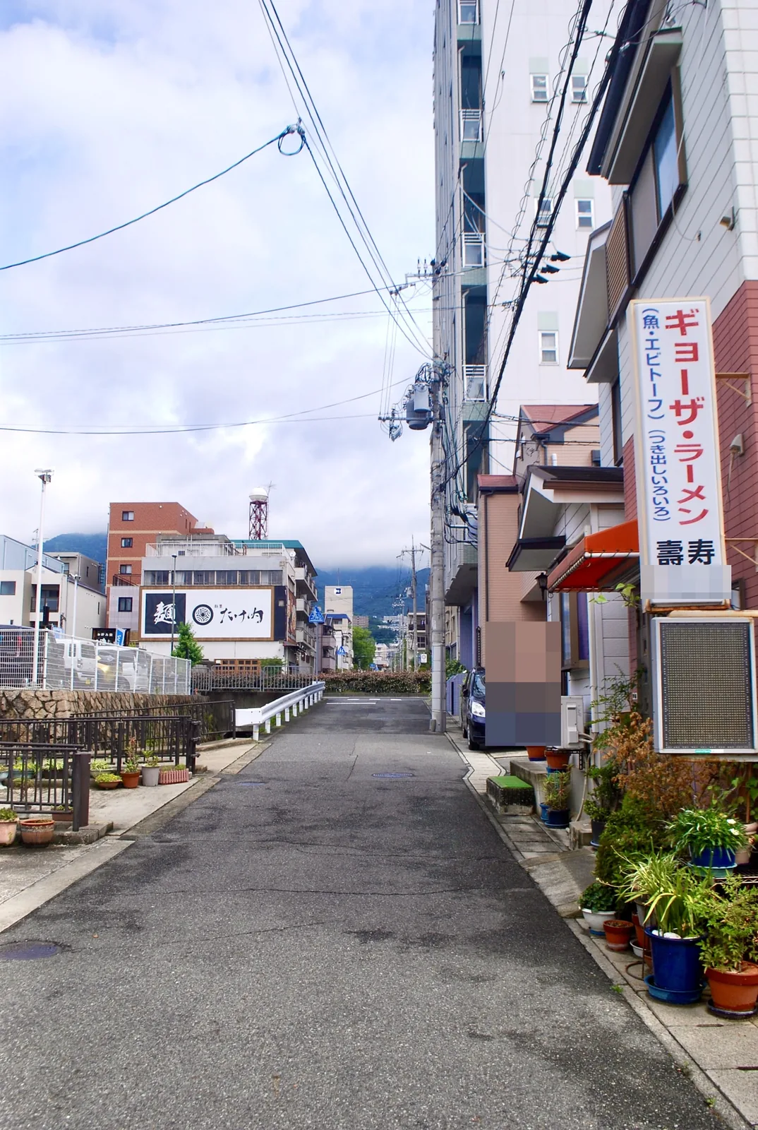 中華料理店の縦長の看板と植木鉢が並ぶ、山へ向かう道