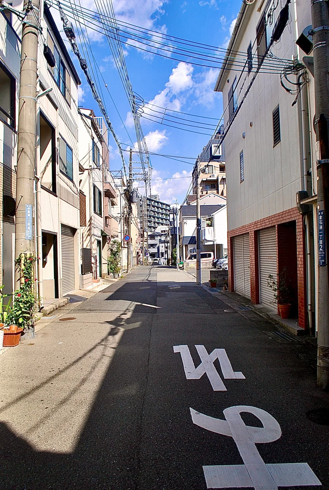 電柱と住宅が並ぶ、日差しと影のある静かな裏通り
