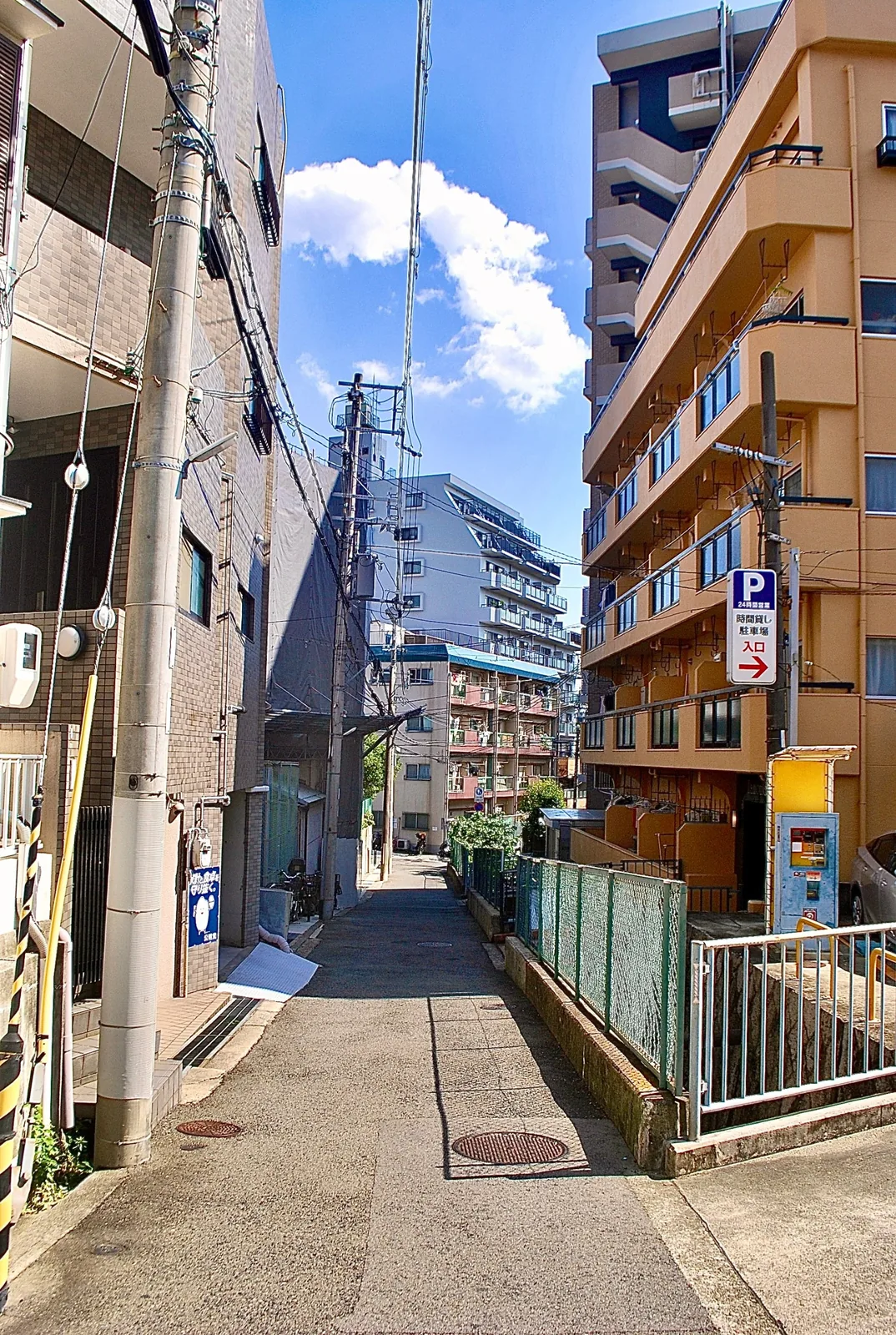 駐車場の看板のある建物の脇を抜ける、細い路地