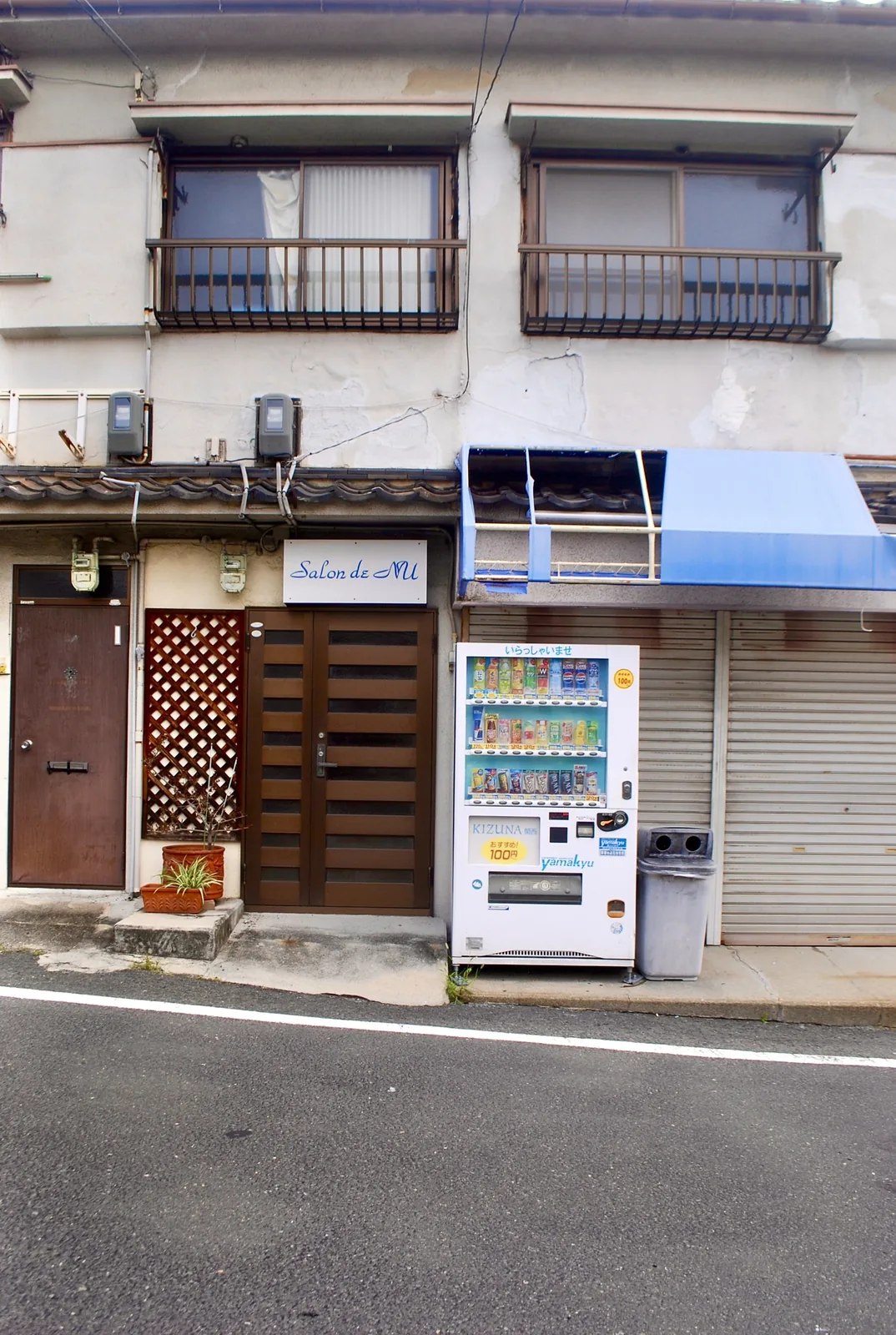 木の格子の扉と青い日よけ、自動販売機の並ぶ古い建物