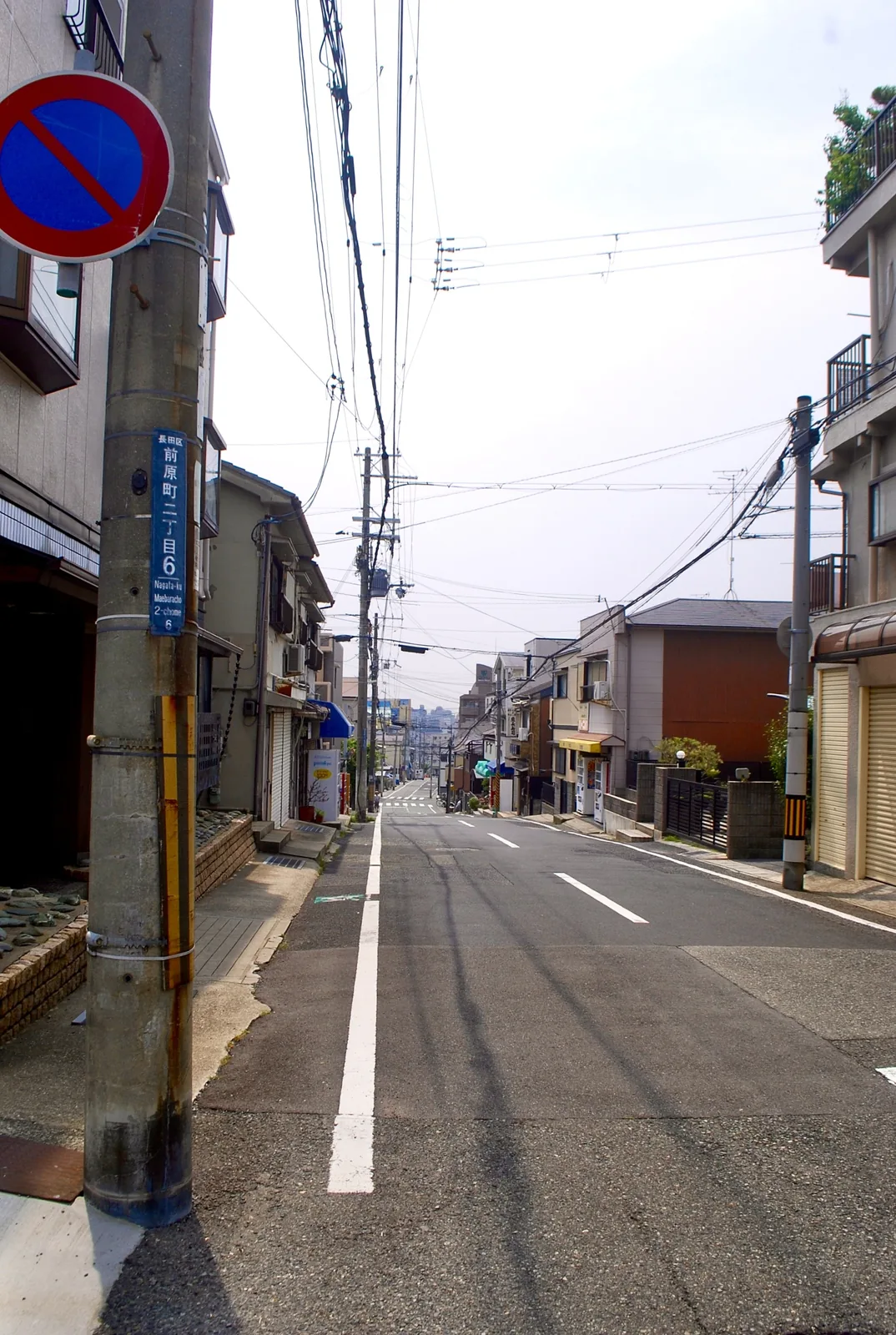 「前原町二丁目」の電柱の先に、遠くまで続く坂道