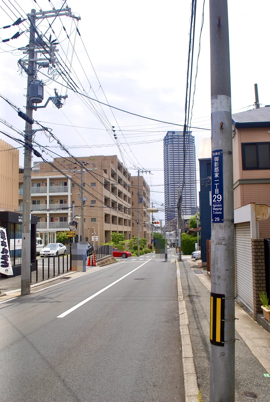 町名表示のある電柱の脇から、高層マンションの見える通り