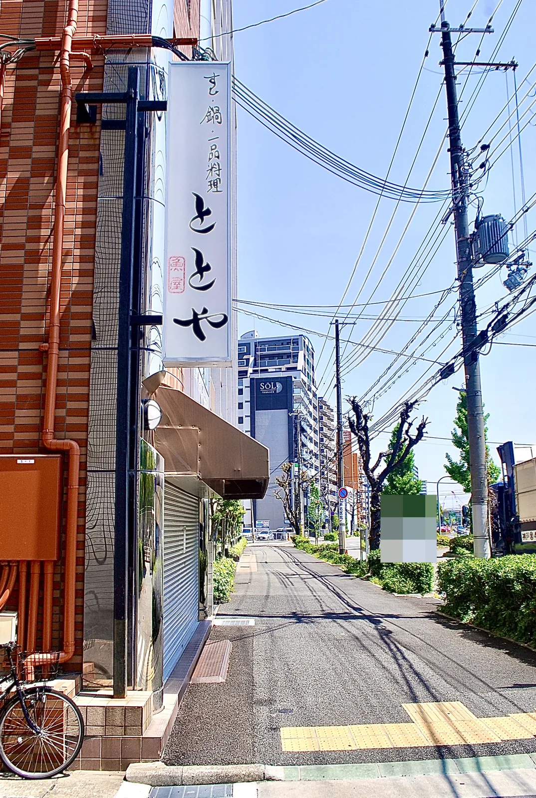 「とと屋」の縦看板のレンガの建物と、並木の続く通り