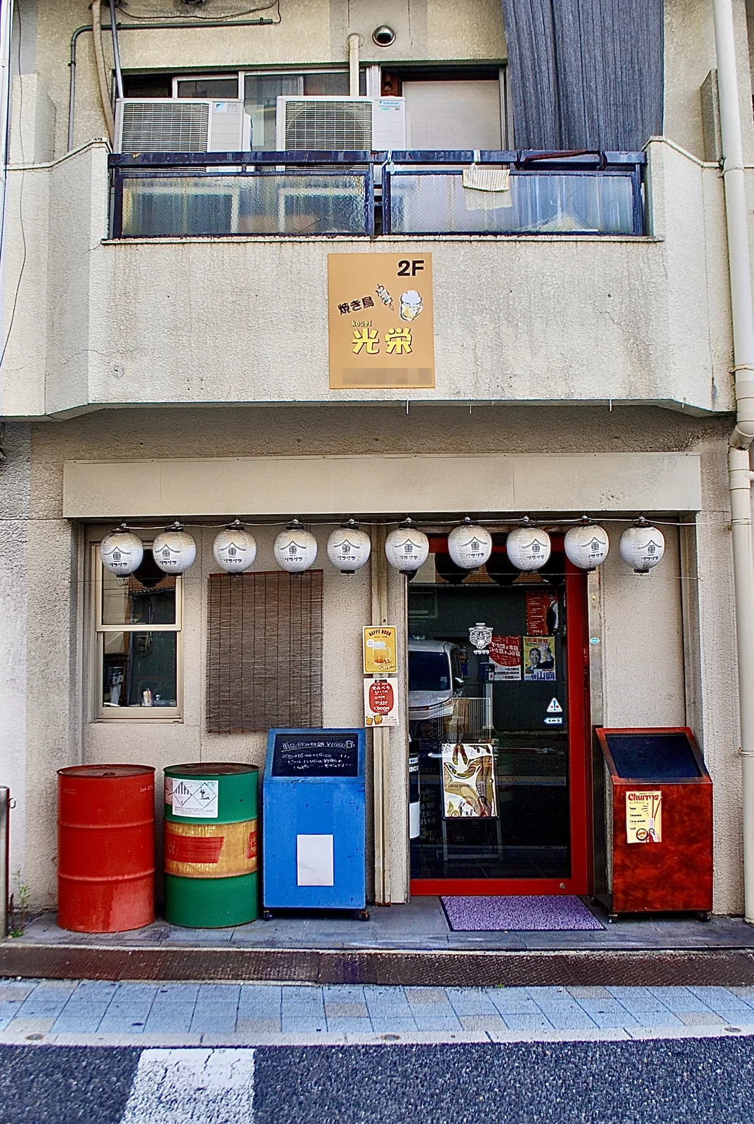 白い提灯と色とりどりのドラム缶が並ぶ、居酒屋の店先
