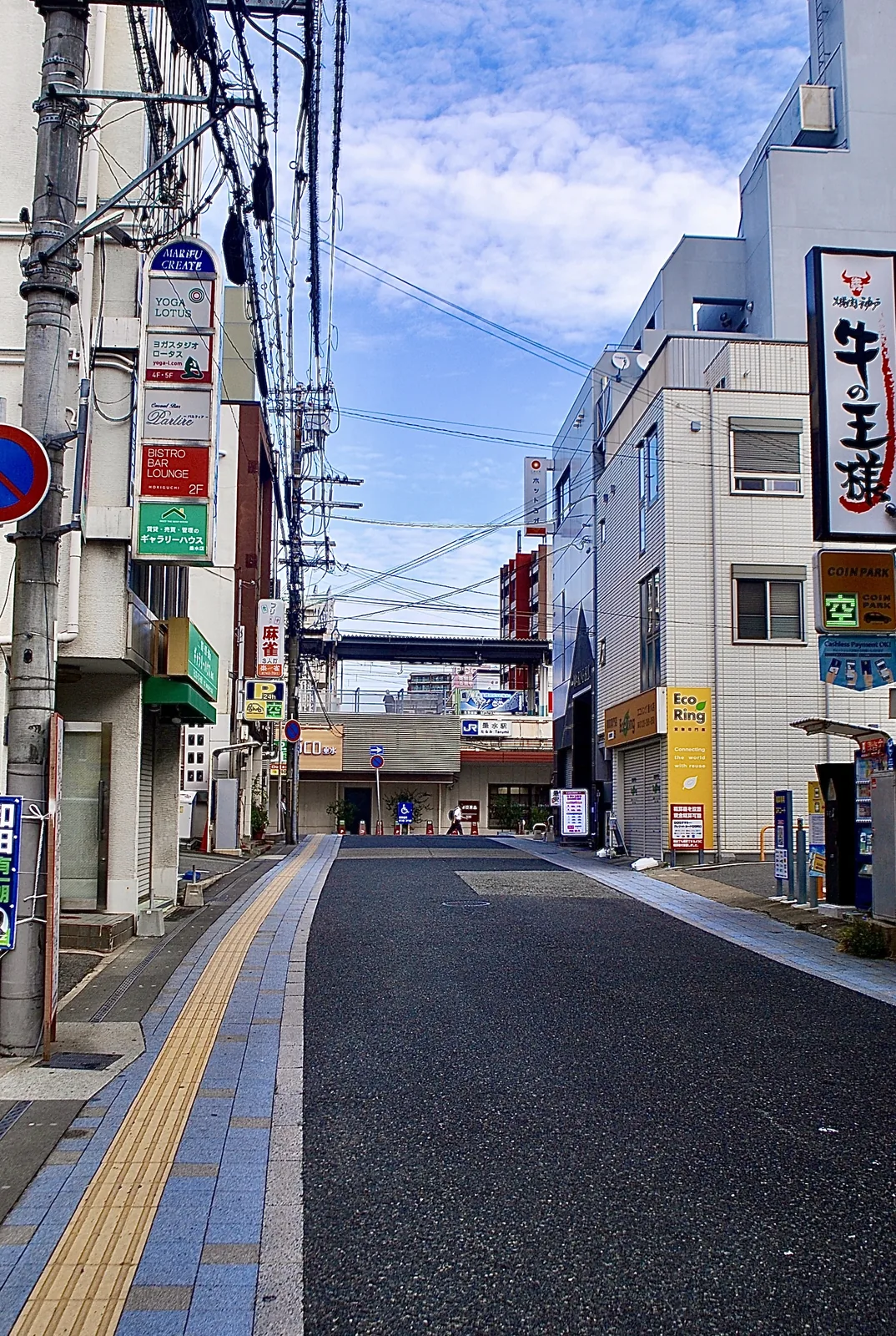 縦長の看板と電線が並び、奥へ続く駅前の通り