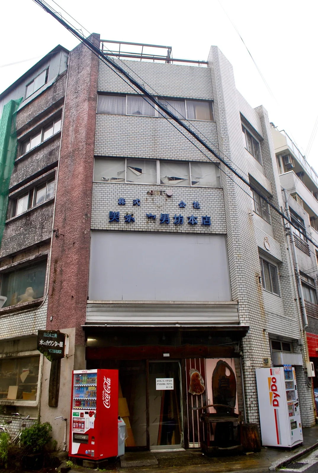 看板文字の残る古いビルの一階に、木のカウンターの工房がある風景