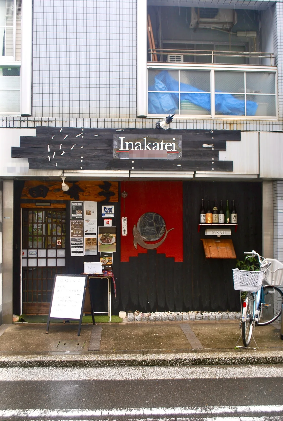 黒い板壁に魚の飾りが泳ぐ、居酒屋の店先