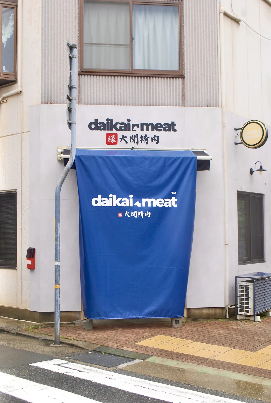 青い幕が下がる精肉店の外壁と、細い電柱