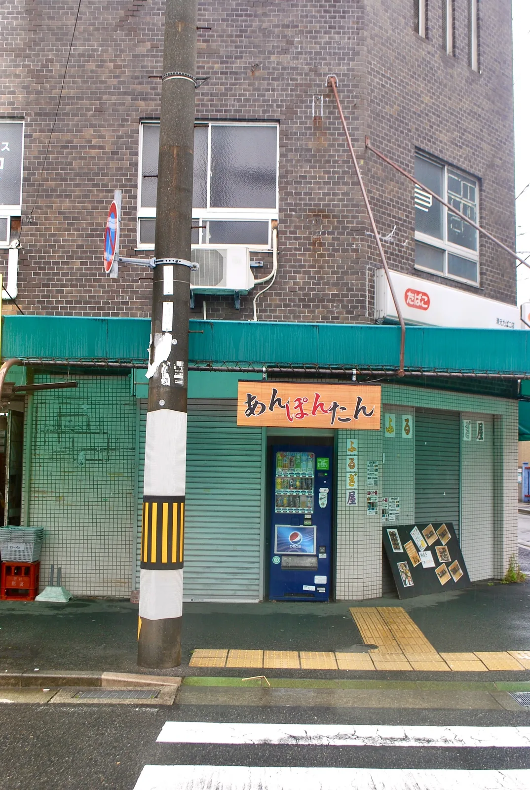 緑の日よけと、シャッターの下りた古い店の並び