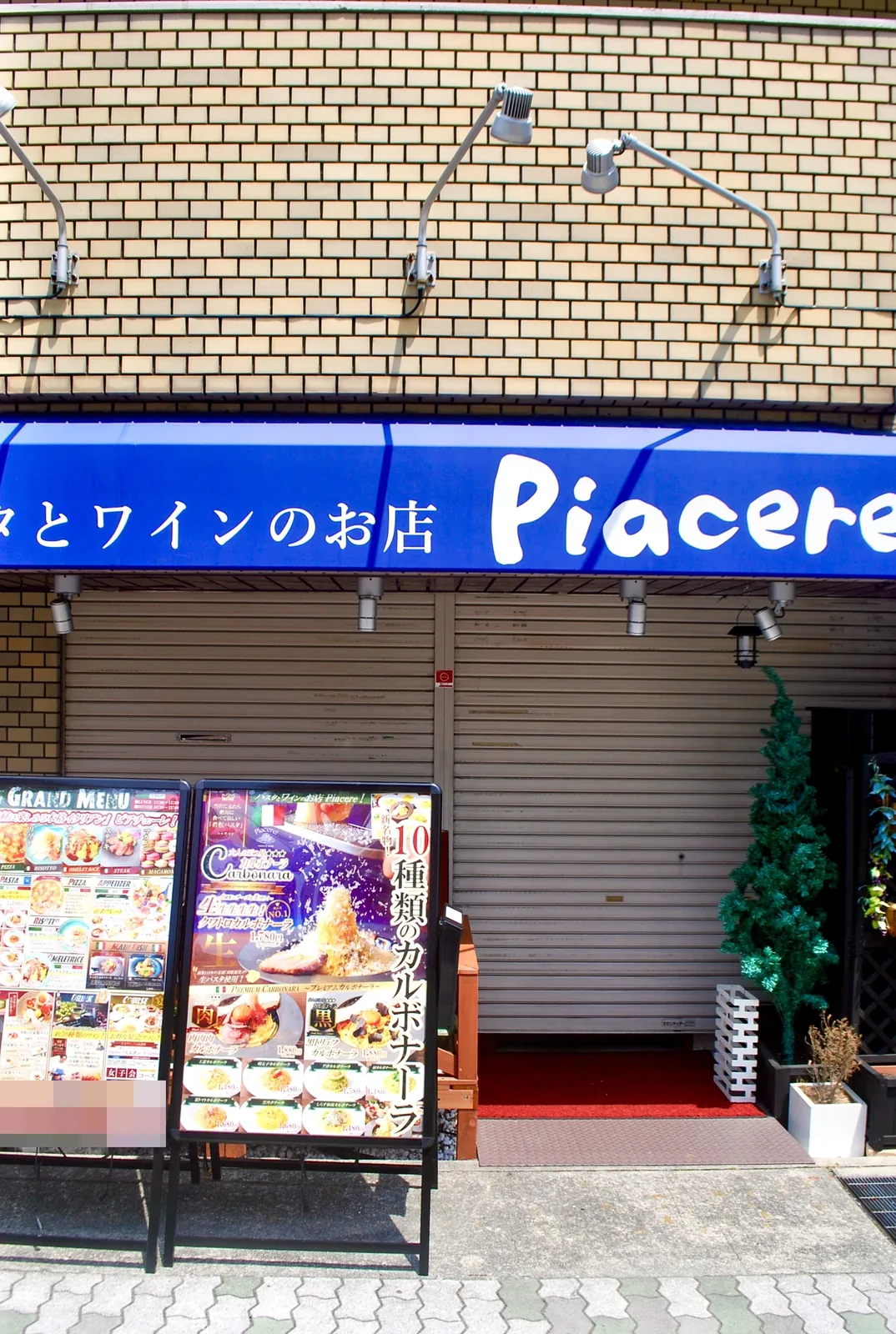 青い日よけと、たくさんのメニューの看板が並ぶパスタの店