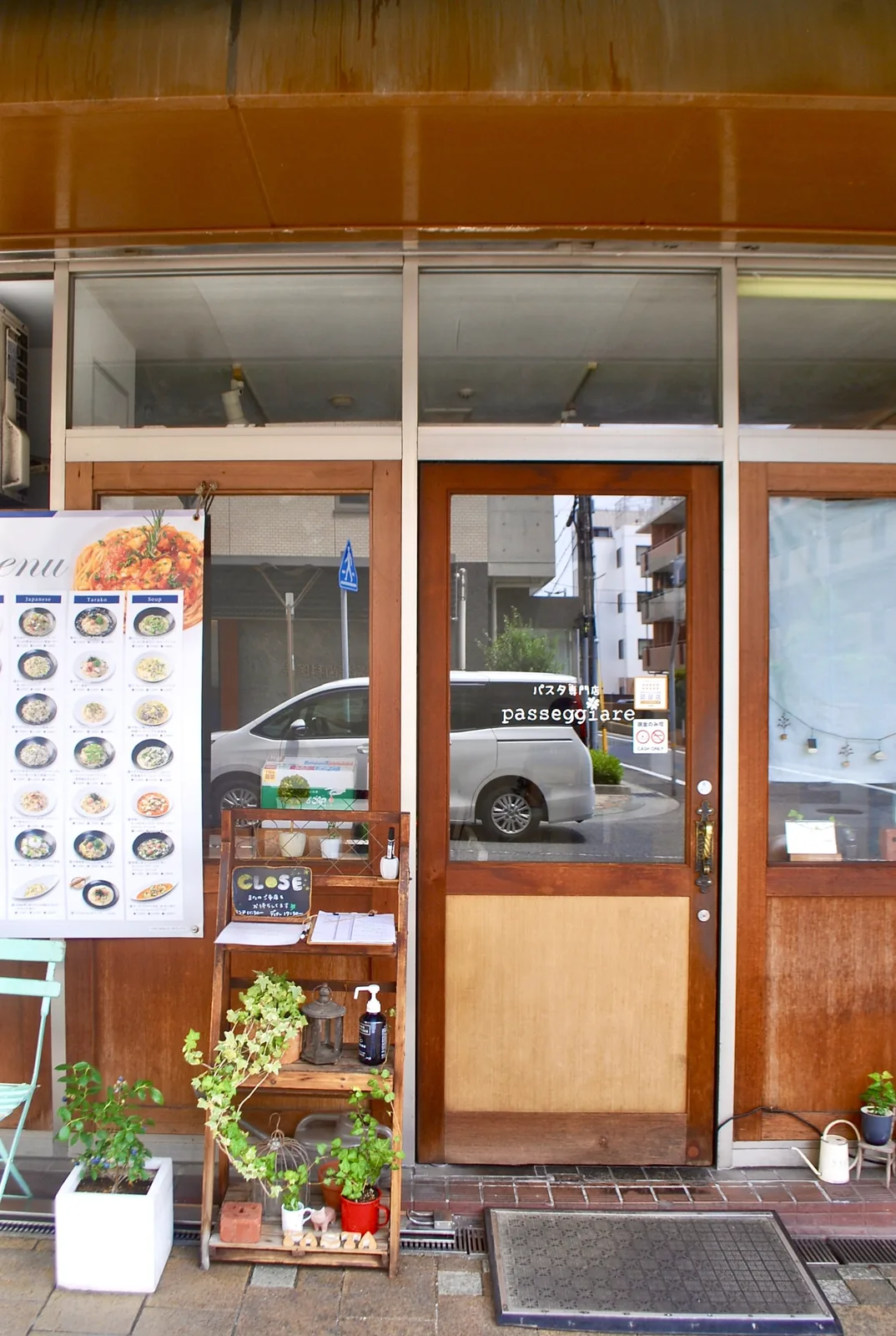 木の扉と窓辺にメニューと植木の並ぶ、パスタ専門店の入口
