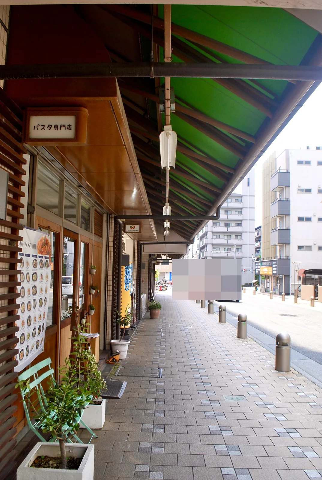 緑の屋根の下を、車止めの並ぶ通りに沿って続く歩道