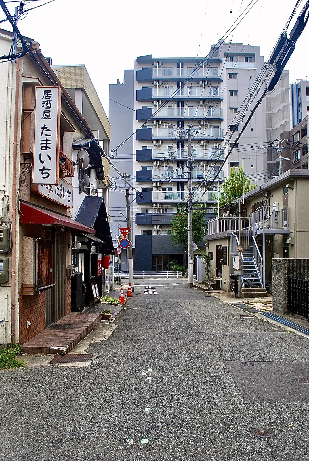 居酒屋「たまいち」の看板と、マンションの見える細い道