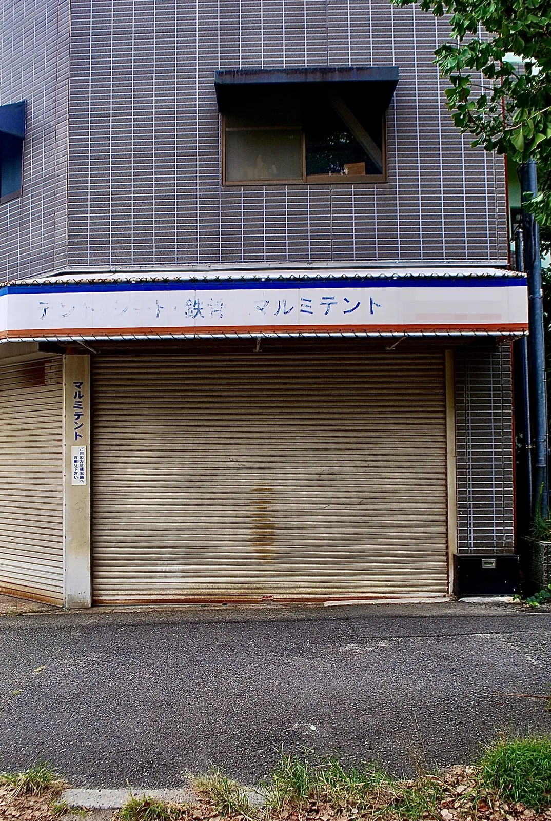 「マルミテント」の看板と、古いシャッターが残る店