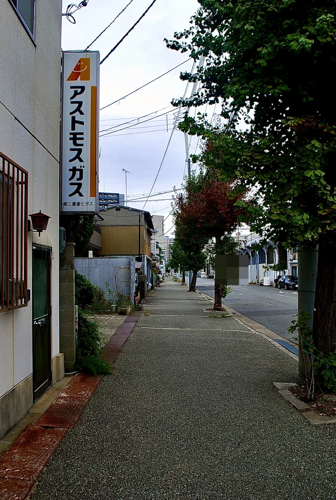 黄色い「アストモスガス」の看板と、並木の続く歩道
