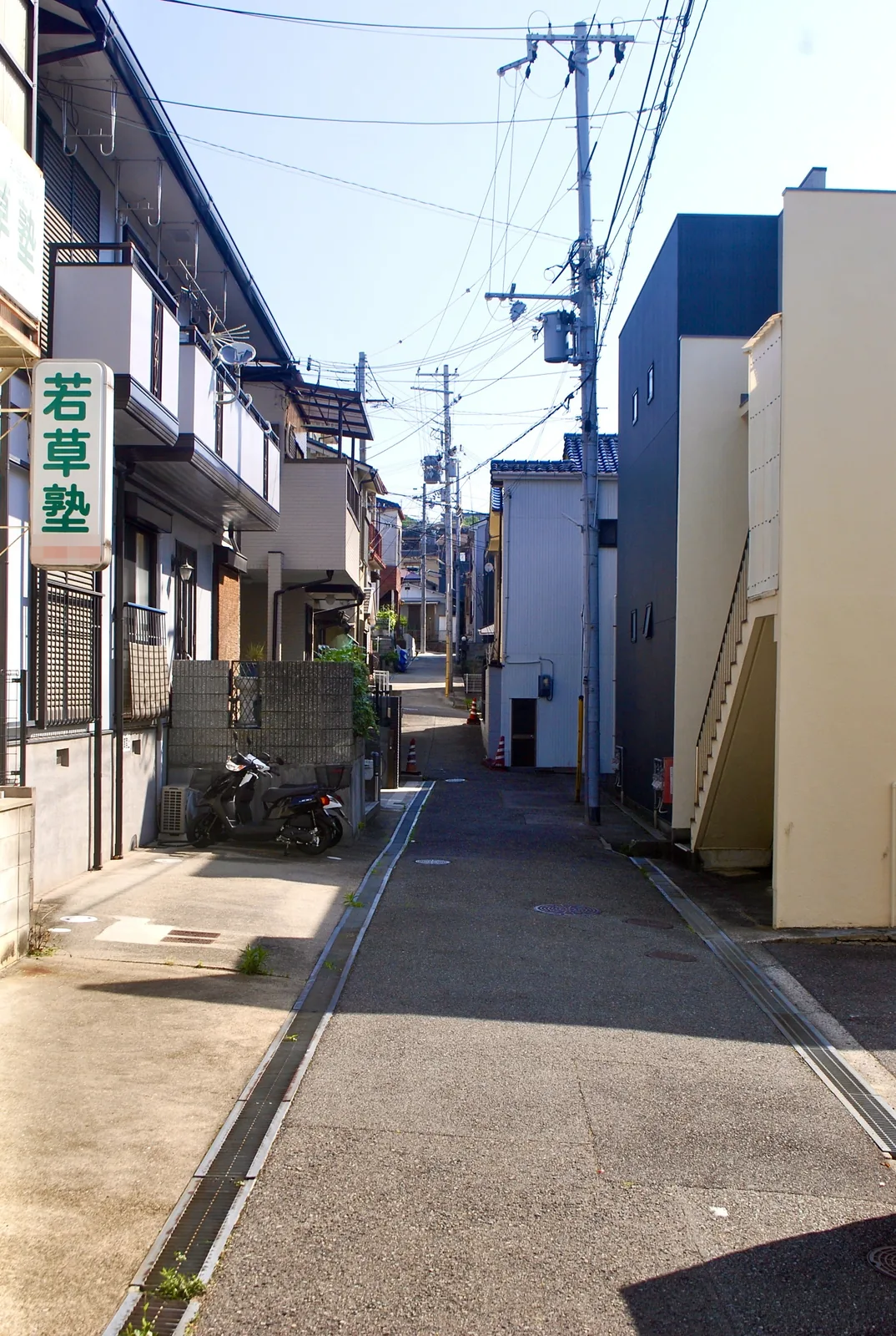縦長の塾の看板と、家々のあいだを奥へ続く細い通り