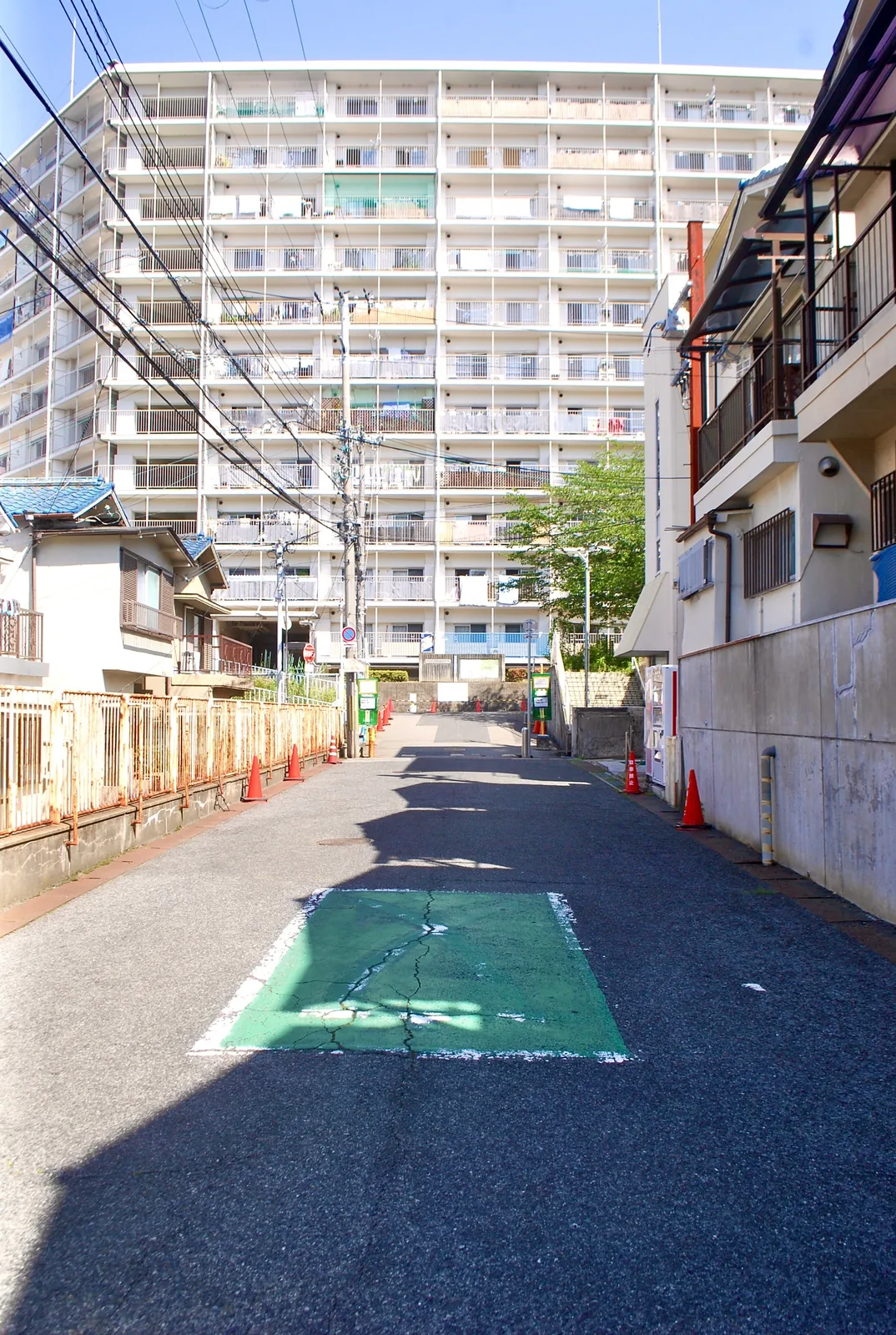 フェンス沿いのまっすぐな道の先に、大きな団地が見える風景