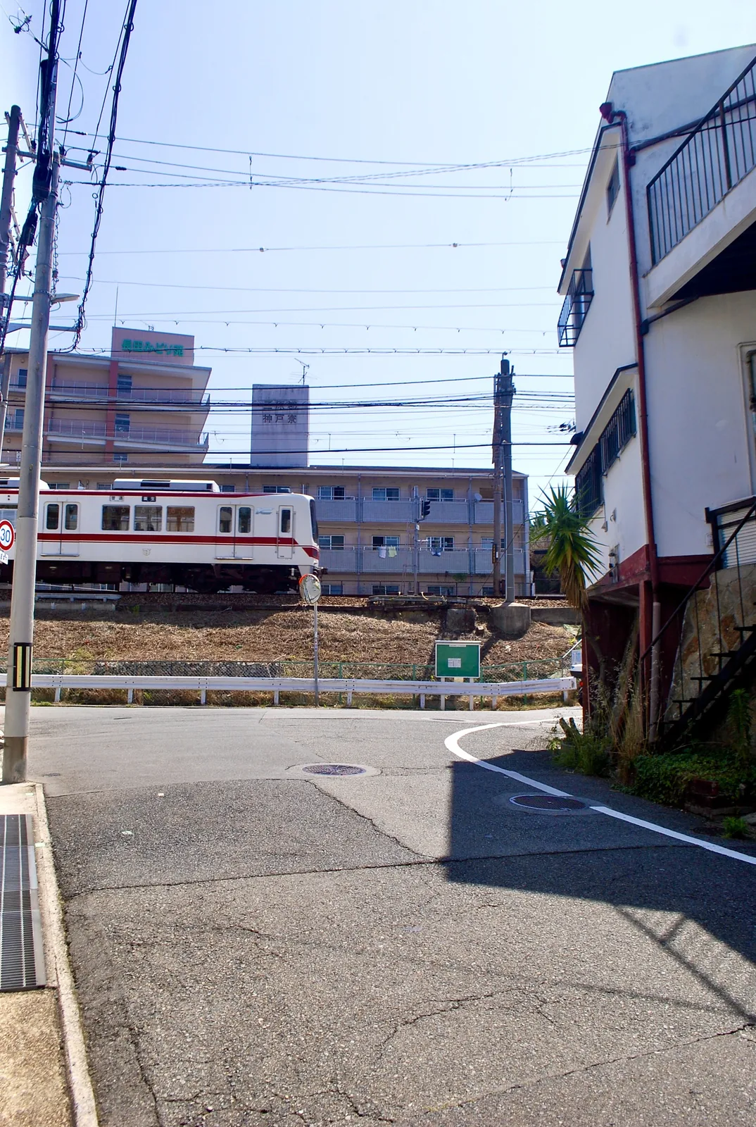 交差点の先の線路を、神戸電鉄の電車が走る風景