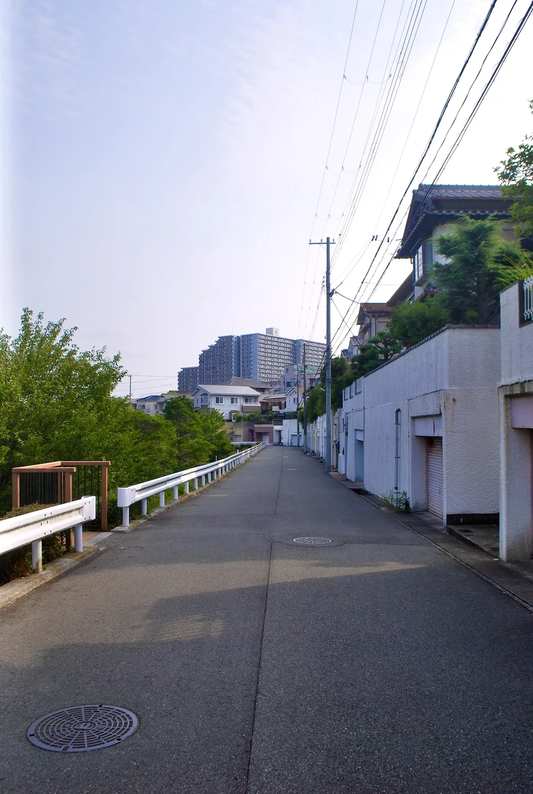 ガードレールと木々に沿って、高層住宅の方へ続く坂道