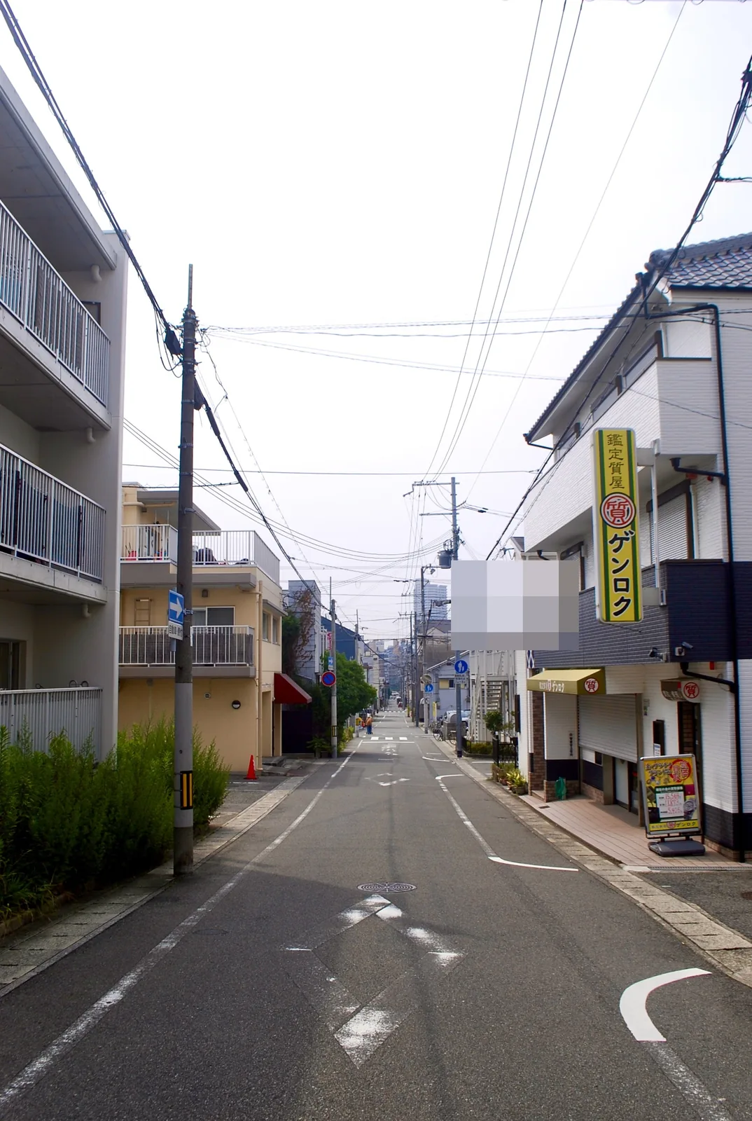 黄色い「質屋」の看板と電柱の並ぶ、まっすぐな住宅街の道