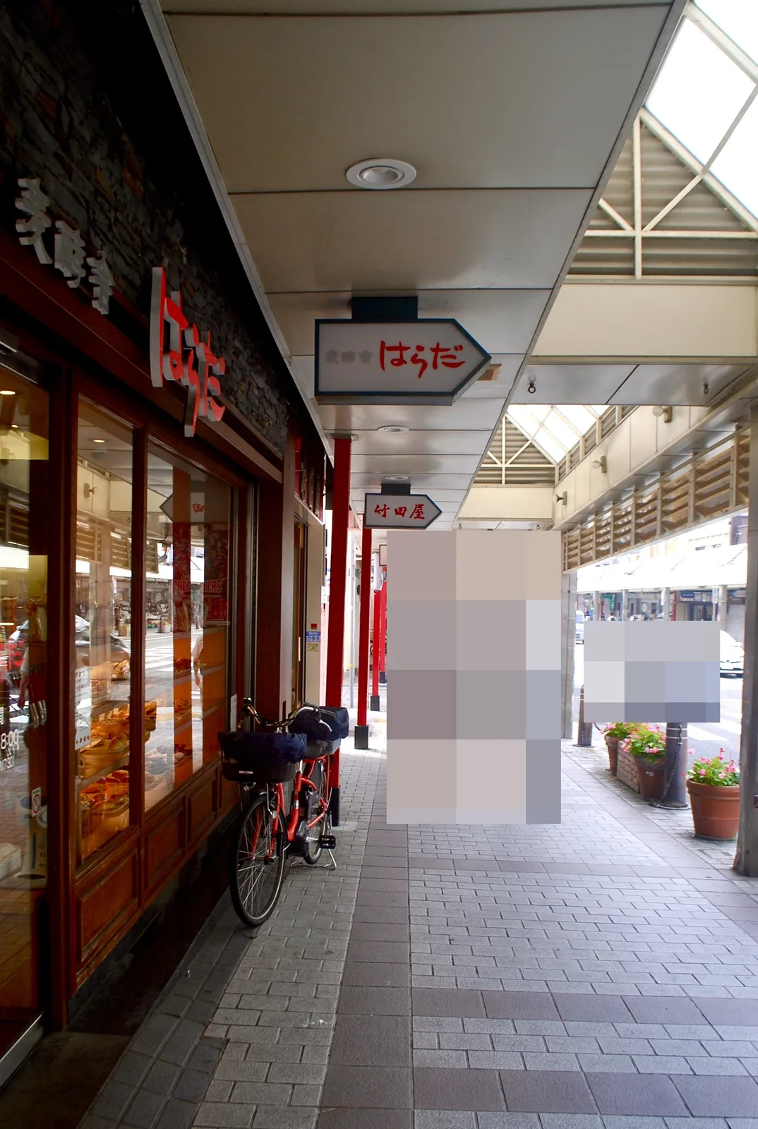 パンの並ぶ大きな窓と自転車、矢印形の看板が続く商店街