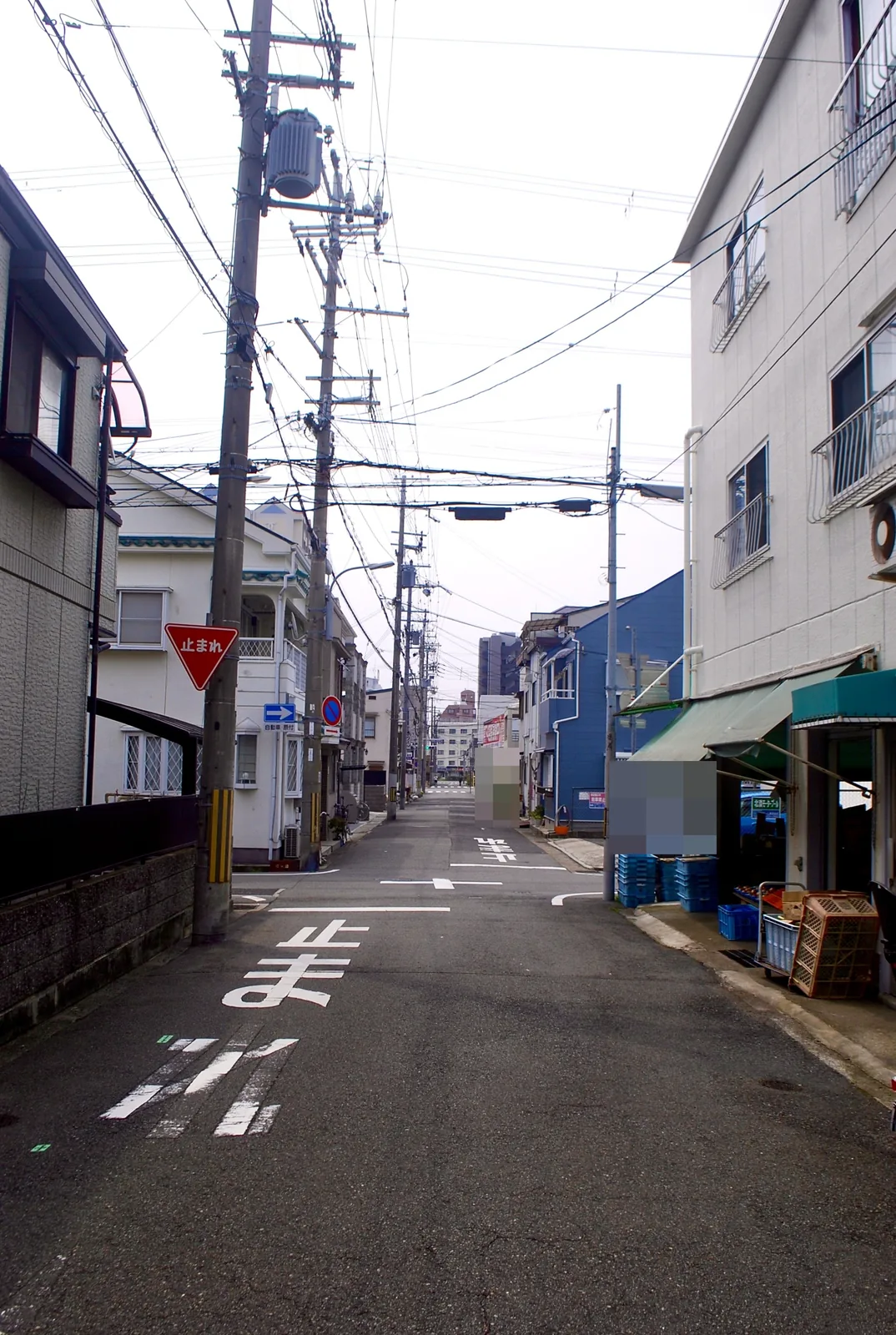 緑の日よけとコンテナの並ぶ店先と、住宅街の交差点