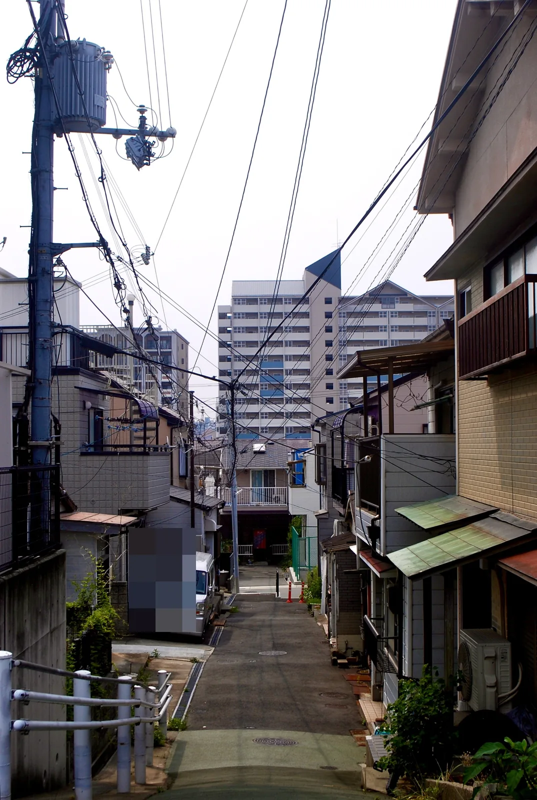 高台から、家々と車の止まる細い路地を見下ろす風景