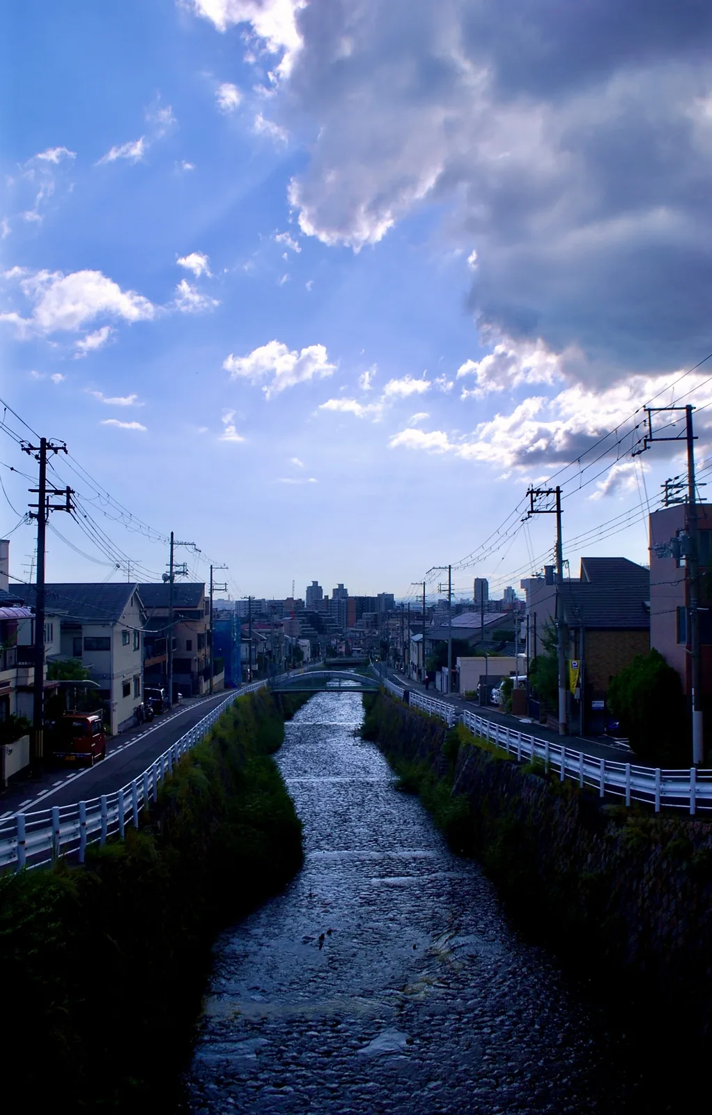 雲の広がる空の下、石積みの川がまっすぐ街並みへと続く風景