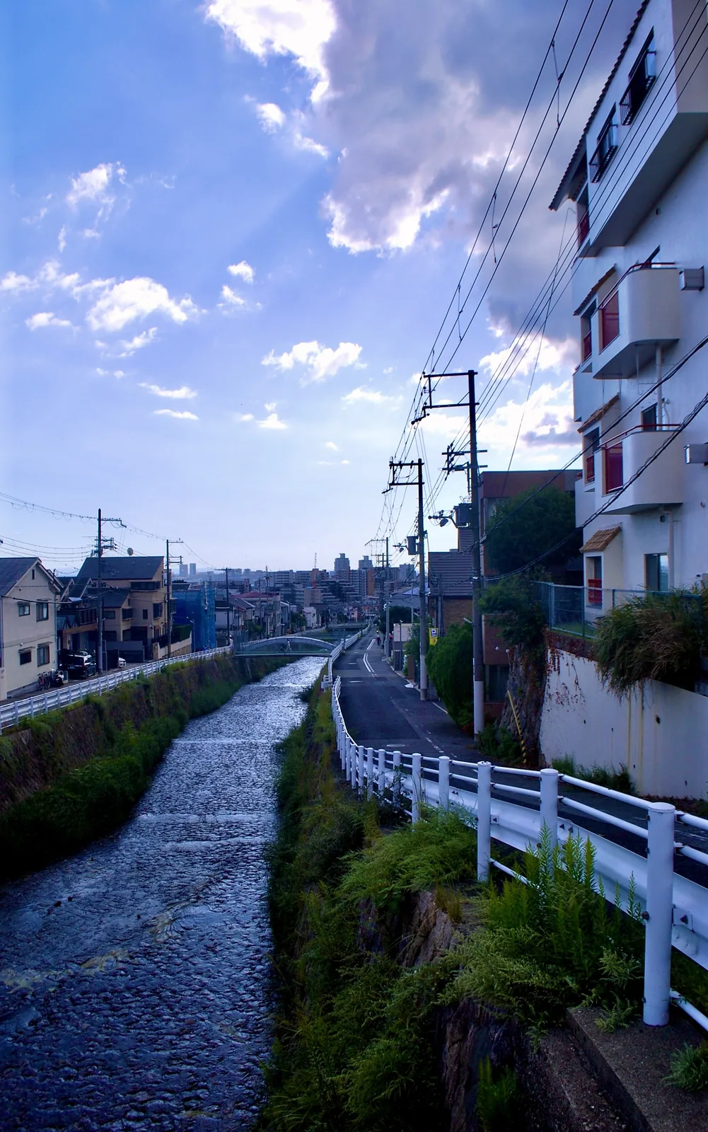 川と並んで続く道の先に、遠くの街並みが見える風景