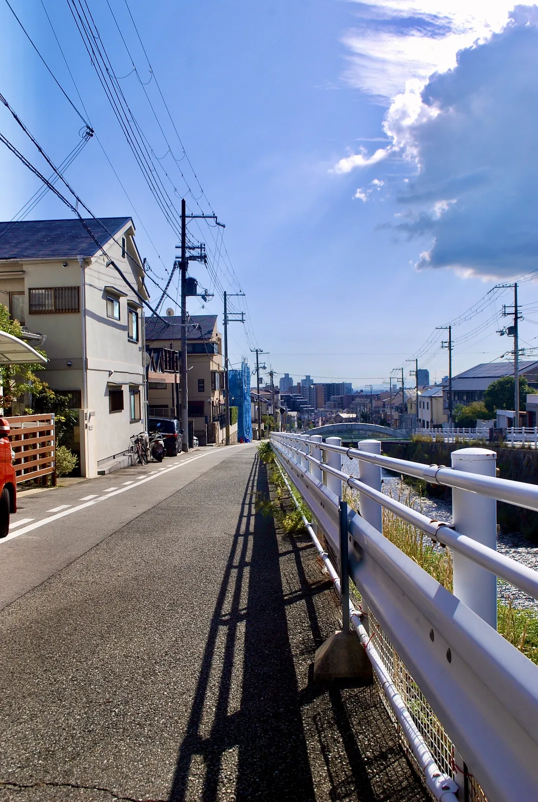 白いガードレールに沿って、川と街並みの方へ続く道