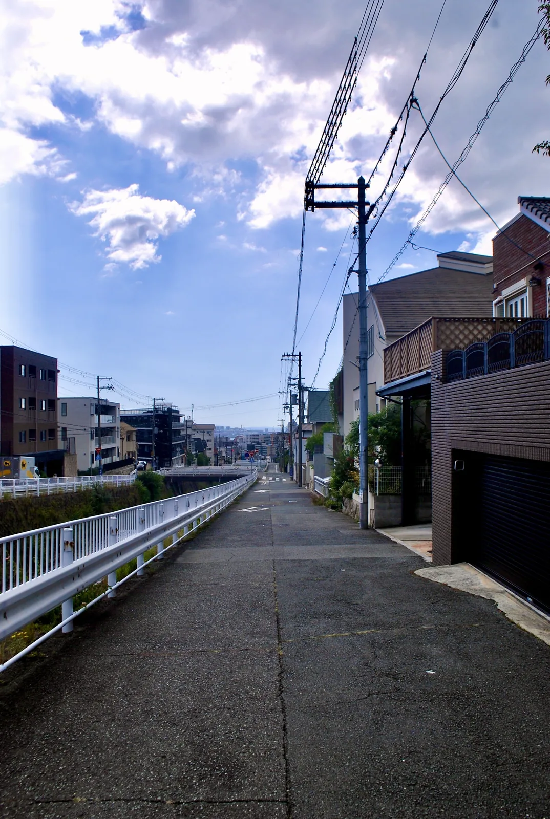 川沿いのガードレールに沿って下っていく道と、空に広がる雲