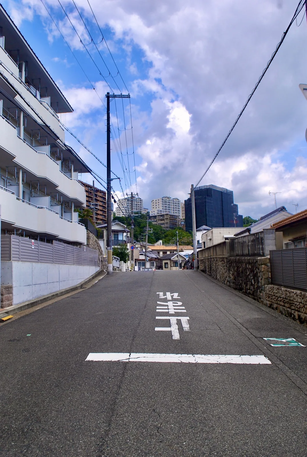 路面に「止まれ」と書かれた坂の先に、町並みと高い建物が見える風景